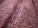 Large mosaic wall art with diagonal stripes in plum, copper, and mahogany tones, creating a warm and elegant abstract design for modern interiors